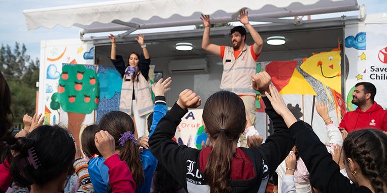 Save the Children staff in Türkiye dance on the stage as children below follow along. Save the Children staff in Türkiye dance on the stage as children below follow along.
