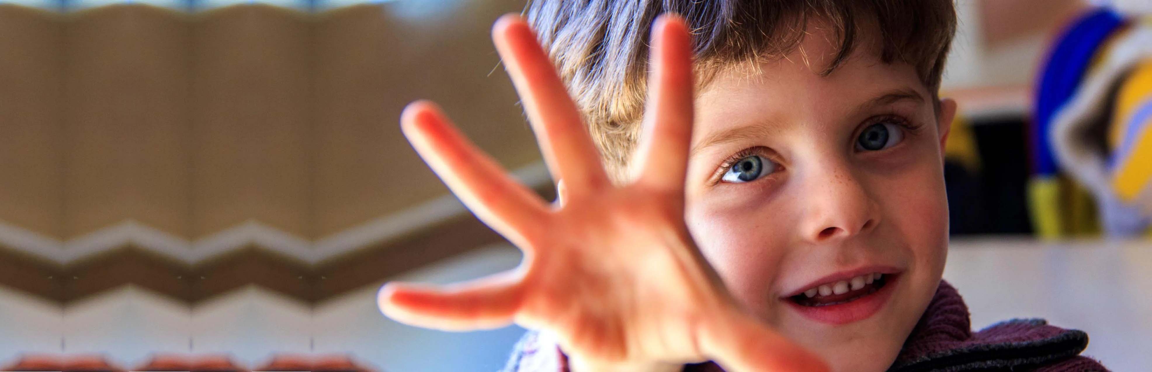 A boy holds his hand up to the camera, as if playing a game.