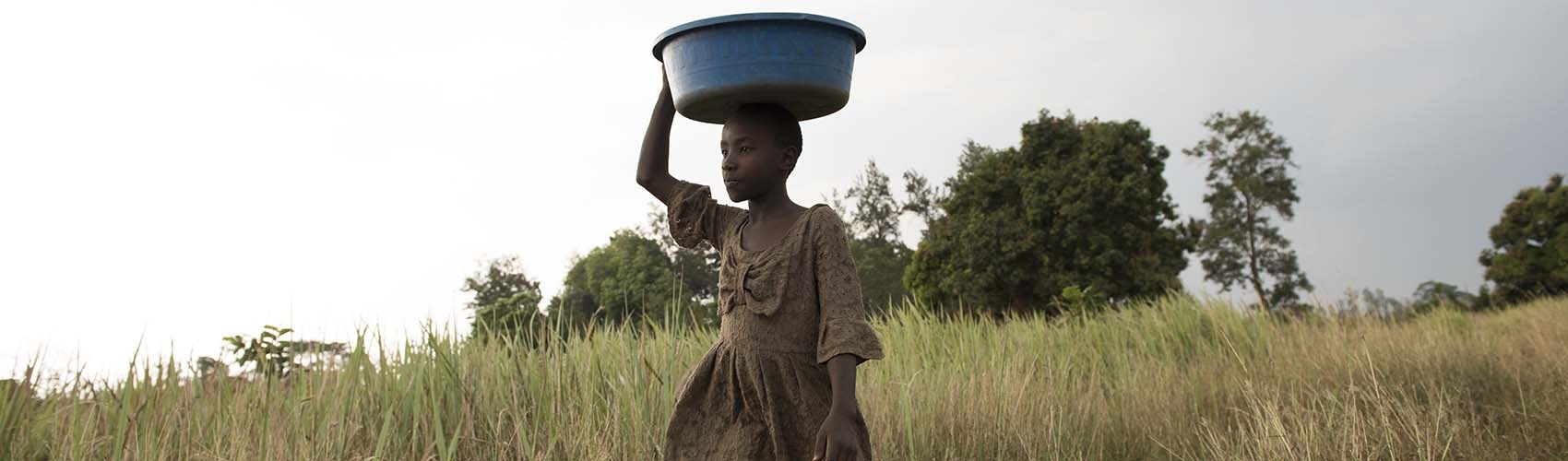 A girl carries a bucket of animal food over her head. A girl carries a bucket of animal food over her head.