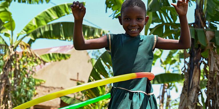 A cheerful little girl in a green dress plays with her hula hoop. A cheerful little girl in a green dress plays with her hula hoop.