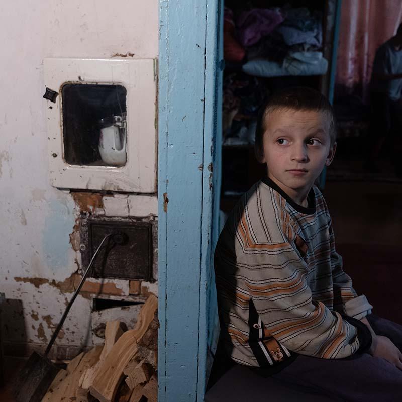 In Ukraine, a young boy sits against a wall in a dark room where his family has been displaced by conflict.