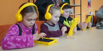 Three young children in Ukraine play educational games on tablets while wearing yellow headphones Three young children in Ukraine play educational games on tablets while wearing yellow headphones