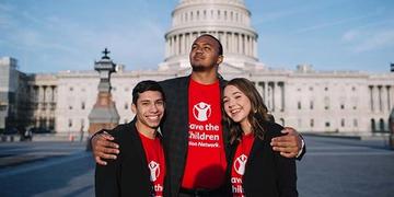 A group of three Student Ambassadors wearing red Save the Children Action Network shirts stand together in front of Capitol Hill during the 2019 Advocacy Summit. A group of three Student Ambassadors wearing red Save the Children Action Network shirts stand together in front of Capitol Hill during the 2019 Advocacy Summit.