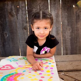 A 3-year old girl named Analia sits at a picnic table outside and displays a colorful painting in front of her. The girl and her mom participated in several learning-based activities taught to them during a home visit as part of Save the Children’s signature Early Steps to School Success program. Photo credit: Save the Children, Nov 2017. A 3-year old girl named Analia sits at a picnic table outside and displays a colorful painting in front of her. The girl and her mom participated in several learning-based activities taught to them during a home visit as part of Save the Children’s signature Early Steps to School Success program. Photo credit: Save the Children, Nov 2017.