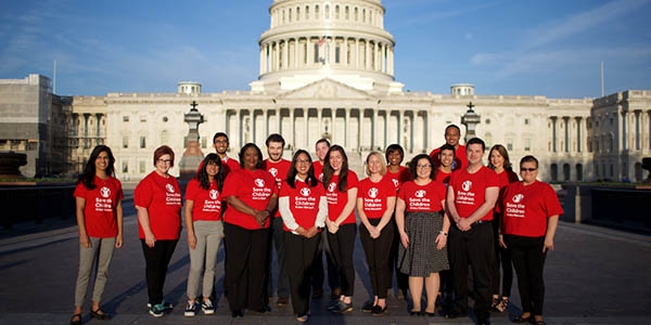A group of Save the Children advocates stand in front of the capital . A group of Save the Children advocates stand in front of the capital .
