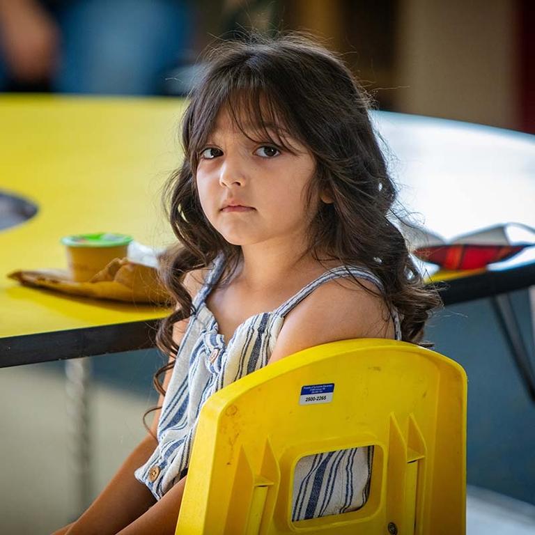A young girl sits at a lunch table in a school cafeteria. A young girl sits at a lunch table in a school cafeteria.