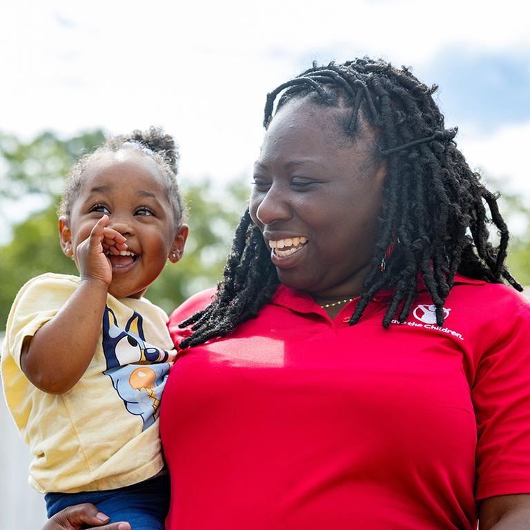 A toddler in the Save the Children mobile classroom program visits with a staff member A toddler in the Save the Children mobile classroom program visits with a staff member