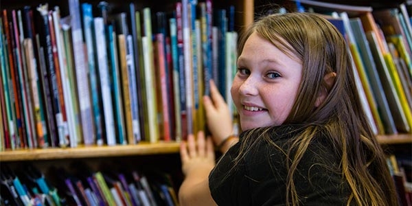 A girl kneels in front of a bookcase and smiles. A girl kneels in front of a bookcase and smiles.