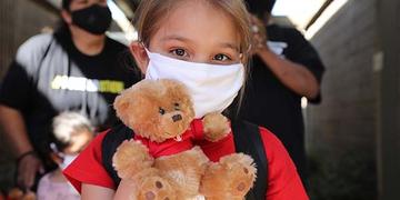A girl wearing a mask holds a teddy bear. A girl wearing a mask holds a teddy bear.