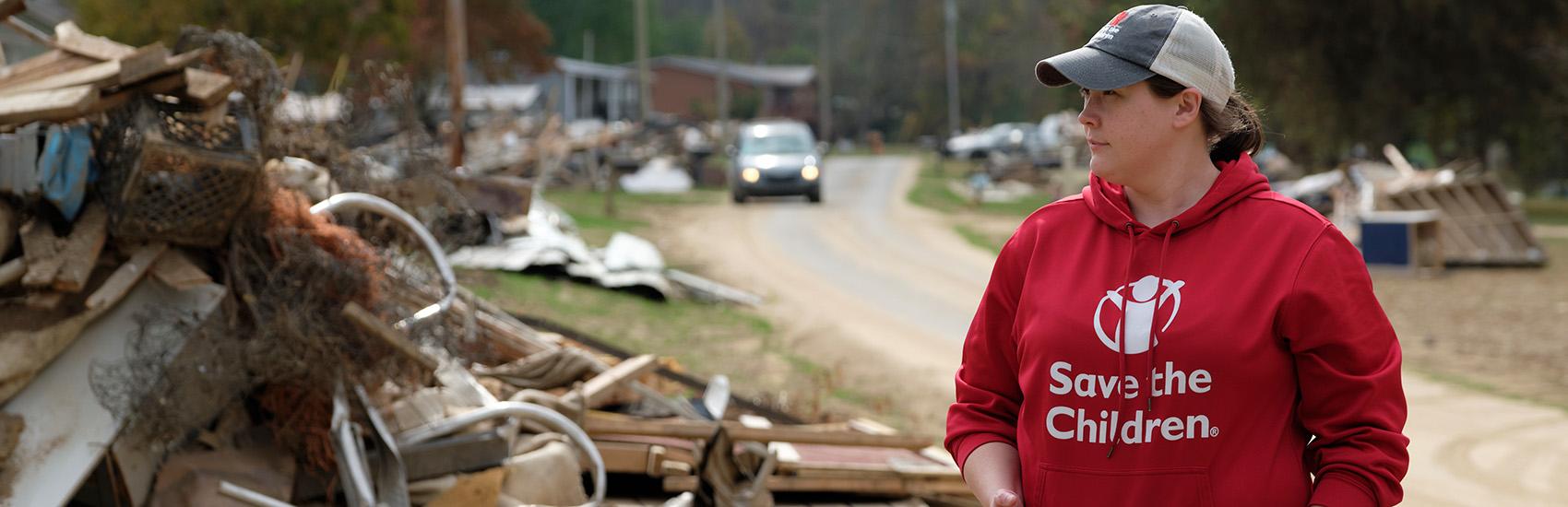 A woman in a baseball hat and red Save the Children sweatshirt brings aid during a disaster