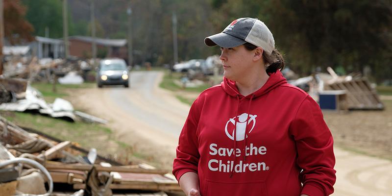 A woman in a baseball hat and red Save the Children sweatshirt brings aid during a disaster