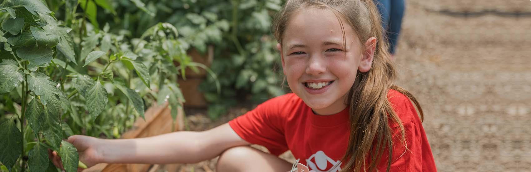 In West Virginia, a young girl kneels near a garden that is part of a summer enrichment learning program that supports early learners in rural communities across the United States.