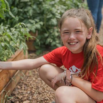 In West Virginia, a young girl kneels near a garden that is part of a summer learning program that supports children in the United States, across rural communities.. In West Virginia, a young girl kneels near a garden that is part of a summer learning program that supports children in the United States, across rural communities..