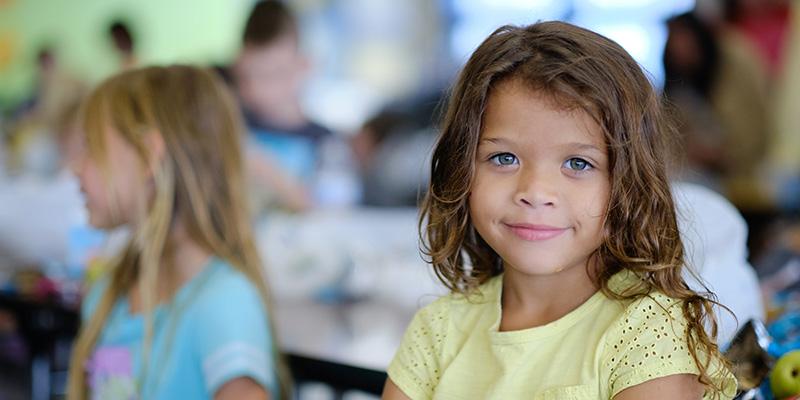 A young girl in a yellow shirt smiles in the cafeteria of her school in Tennessee