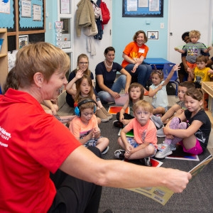 A Save the Children team member reads to a class of young children who are seated on the floor of a classroom. A Save the Children team member reads to a class of young children who are seated on the floor of a classroom.