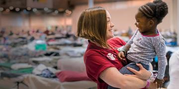 Erin, a Save the Children staff member, smiles at a 2-year old girl in a mega-shelter in Houston. Save the Children distributed cribs and other essentials to families in Texas in the aftermath of Hurricane Harvey. Photo credit: Susan Warner/Save the Children, September 2017. Erin, a Save the Children staff member, smiles at a 2-year old girl in a mega-shelter in Houston. Save the Children distributed cribs and other essentials to families in Texas in the aftermath of Hurricane Harvey. Photo credit: Susan Warner/Save the Children, September 2017.