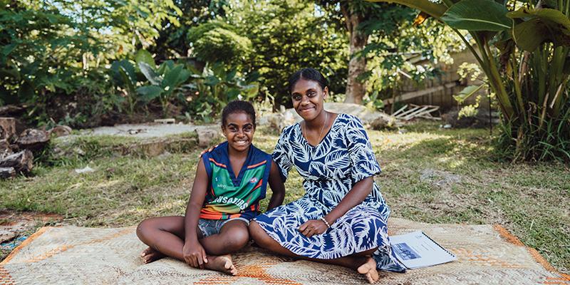 A teenage girl and her younger sister sit on a blanket in Vanuatu A teenage girl and her younger sister sit on a blanket in Vanuatu