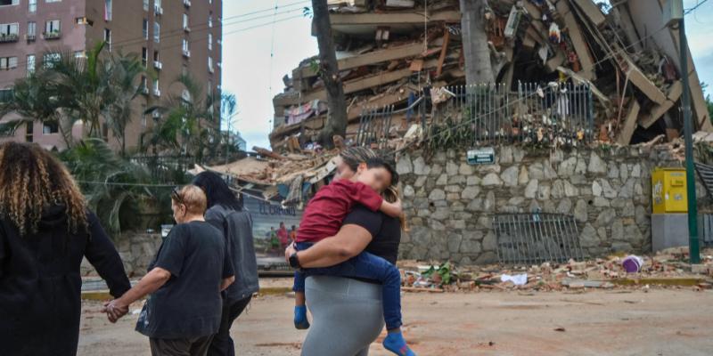 People walk past a collapsed building following an earthquake in Caracas