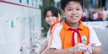 Children in orange school uniforms wash their hands at a handwashing station Children in orange school uniforms wash their hands at a handwashing station