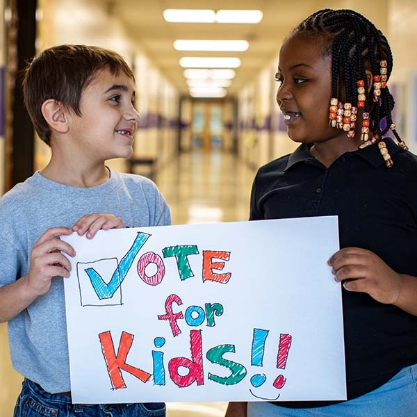 A boy and girl hold a sign that says "Vote for Kids." A boy and girl hold a sign that says "Vote for Kids."