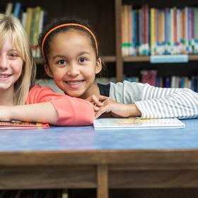 West Viginia, a two girls stand in a library and smile at the camera West Viginia, a two girls stand in a library and smile at the camera
