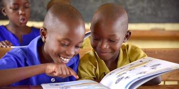 Two children smile as they look at a large book together. Two children smile as they look at a large book together.
